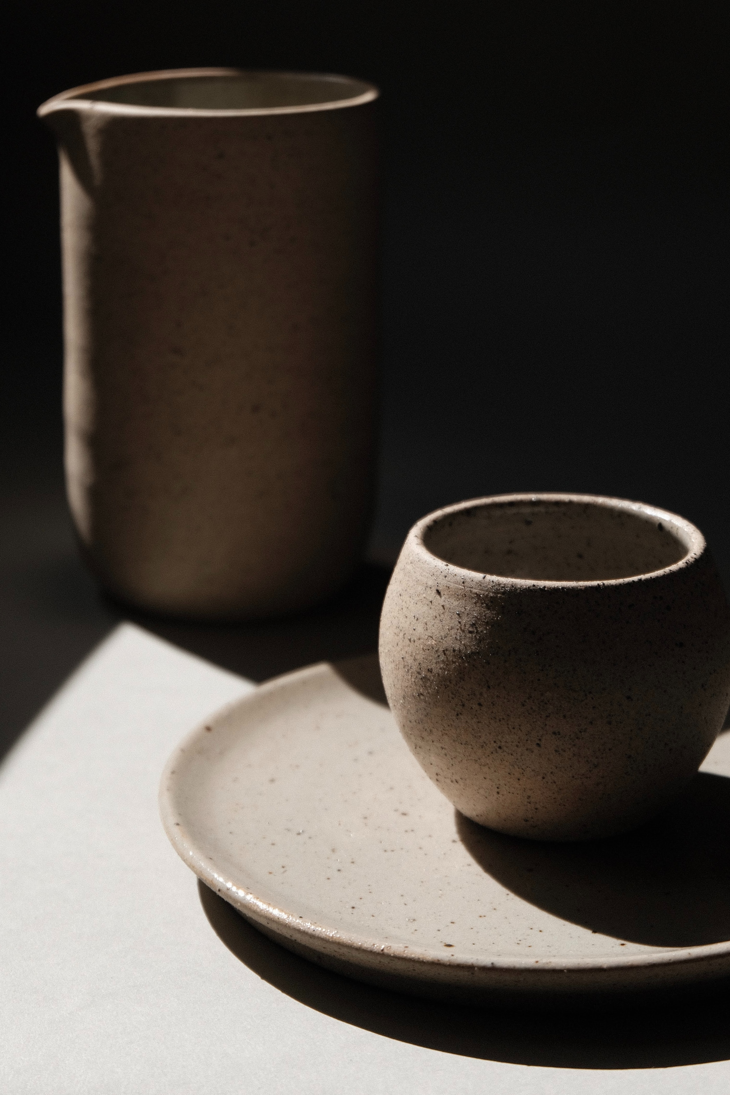 Una jarra, una taza y un plato de cerámica artesanal en colores crudos